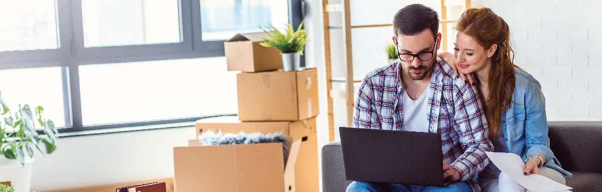 Young couple moving in new home. Sitting and relaxing after unpacking. Searching home decorating ideas on laptop.