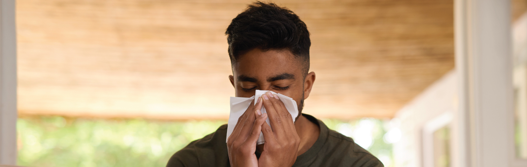 Attractive African American man sneezing due to poor indoor air conditions
