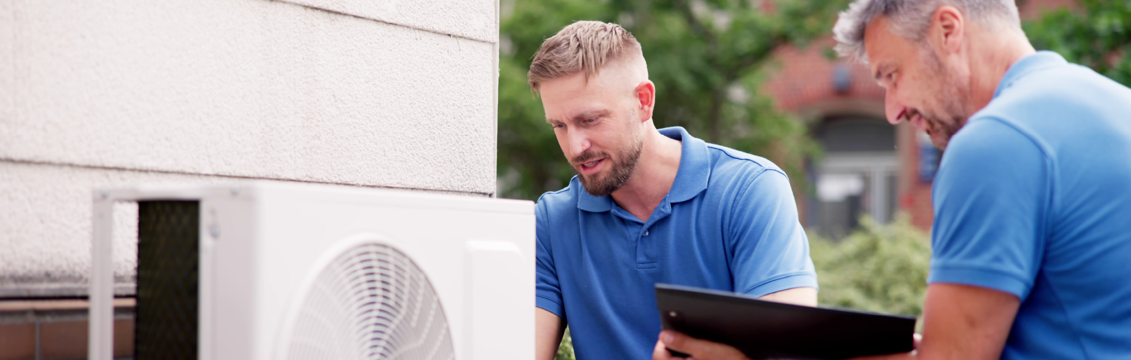 two male HVAC technicians working on an outdoor HVAC unit