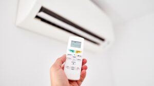 AC tune-up: A hand holding a remote control is pointed at a wall-mounted air conditioner, ready to adjust settings after an ac tune-up.