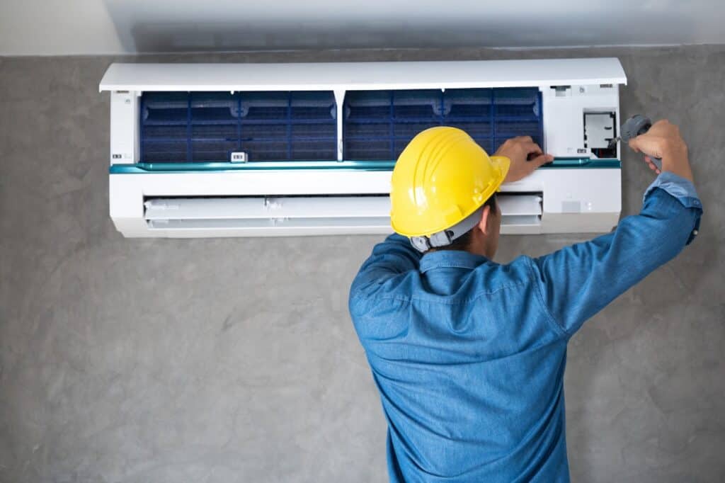 %Title% | Chancey &Amp; Reynolds A person in a yellow hard hat and blue shirt is installing or repairing a wall-mounted air conditioning unit with a screwdriver in Alcoa, TN.