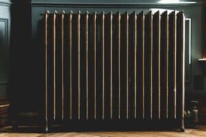 %Imagetitle% | Chancey &Amp; Reynolds An old metal radiator with multiple vertical columns stands against a wall on a wooden floor in a dimly lit room in Alcoa, TN. Residential heating repair