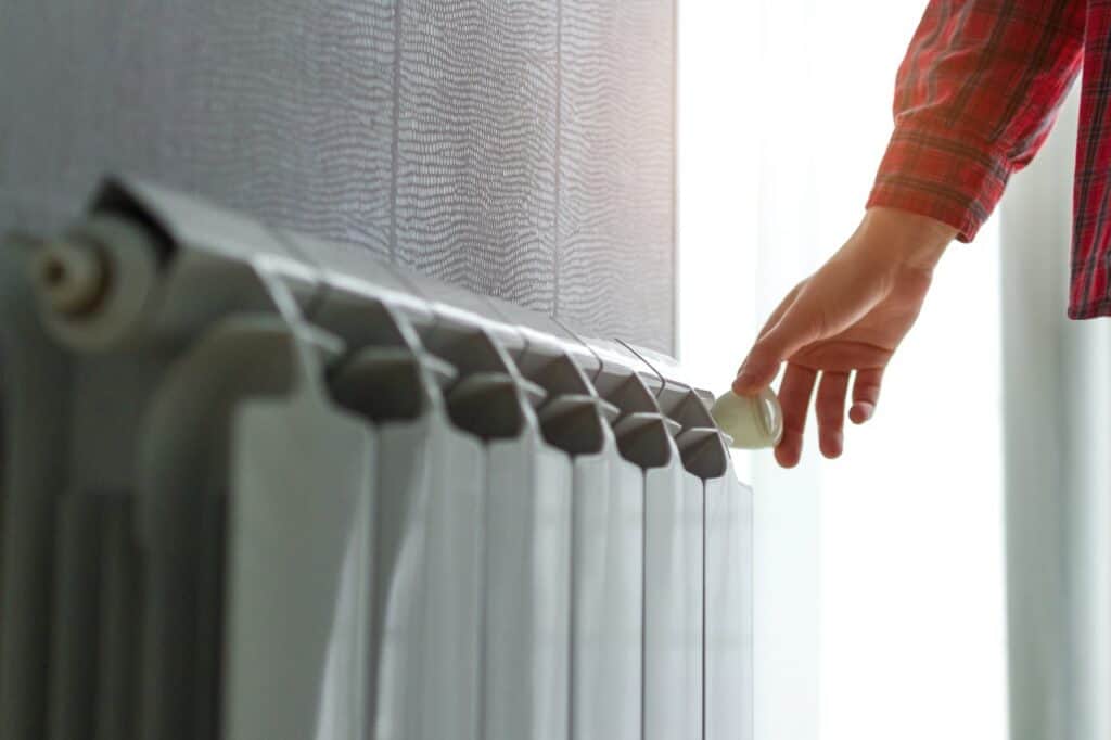 %Title% | Chancey &Amp; Reynolds A person’s hand adjusts the temperature knob on a metal radiator in a sunlit room, evoking a cozy morning scene reminiscent of homes in Alcoa, TN. Heat Pump