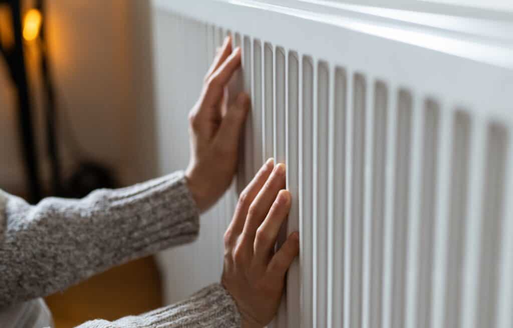 A person in a gray sweater places both hands on a white radiator, warming up on a chilly day in Alcoa, TN.