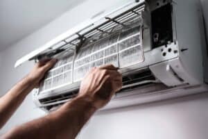 Close-up of a person in Alcoa, TN removing a dirty air filter from a wall-mounted air conditioning unit for cleaning or maintenance. Mini Split Repair Near Me